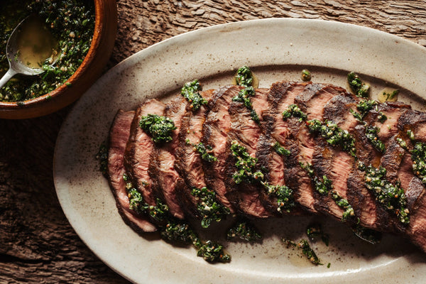 Sliced steak with green herb sauce on a white plate, wooden background