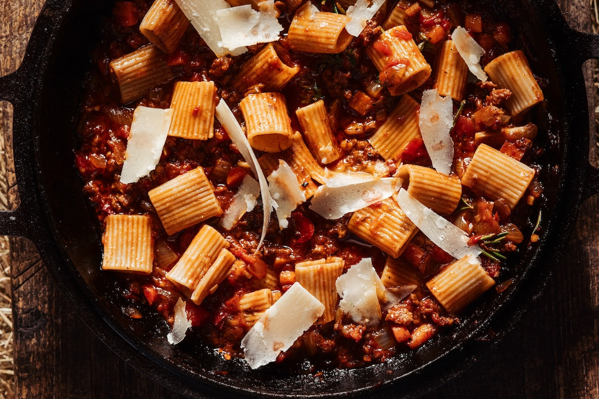 Pasta dish with sauce and parmesan cheese in a black skillet on a wooden surface